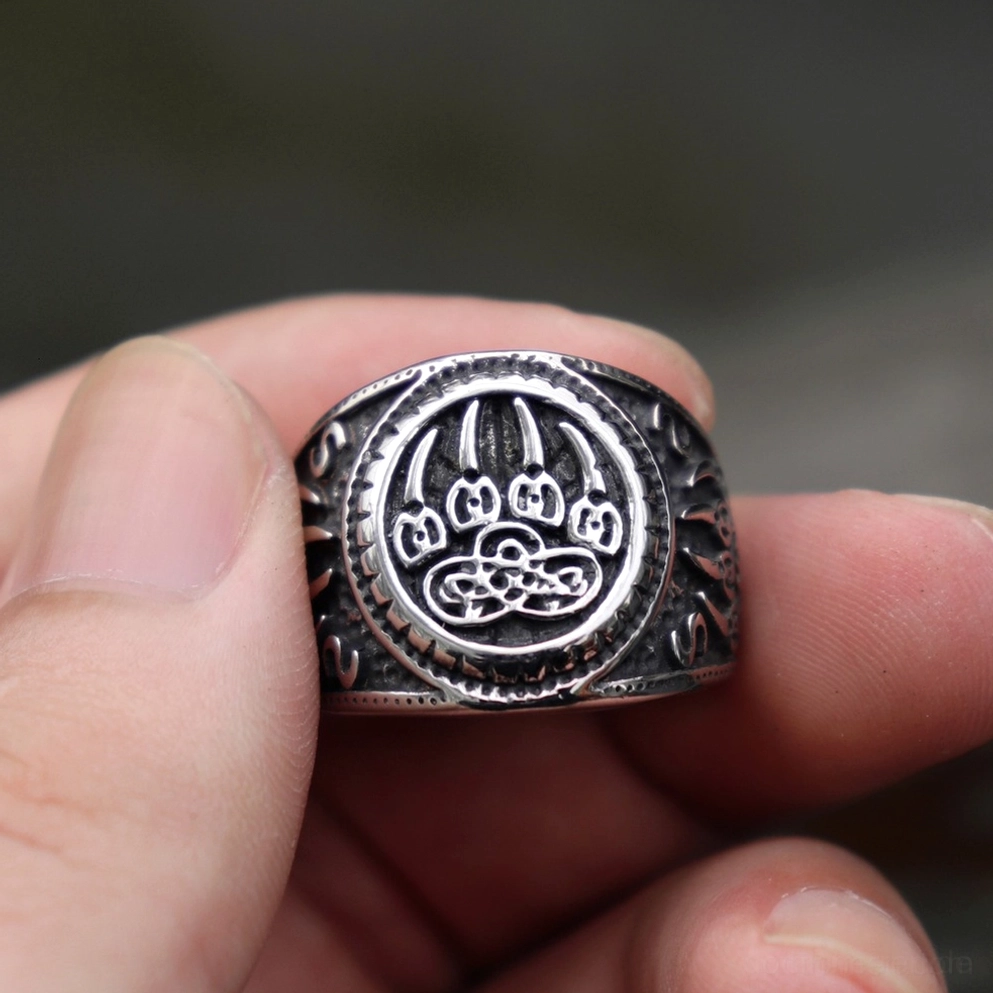 Bärenpfote Keltischer Knoten Gothic Amulett Ring – Vorder-Nahaufnahme in Fingern gehalten zeigt Bärenpfote und keltisches Knotenmuster auf gealterte Edelstahl-Oberfläche