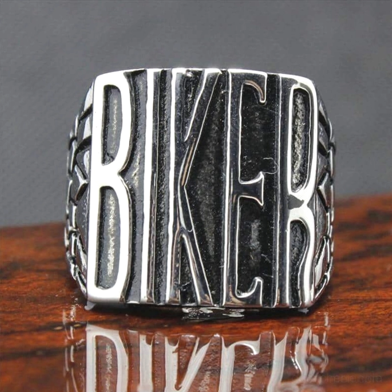 Biker Statement Ring mit polierter Silberfinish und geprägter BIKER Schrift auf reflektierendem Holztisch, authentisches Finish-Display, Draufsicht