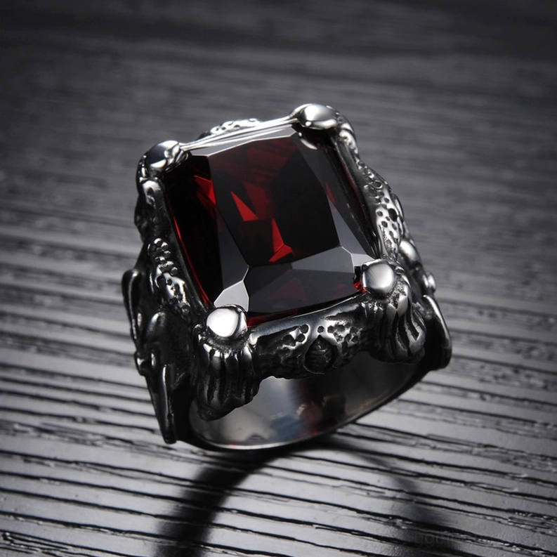 Schräger 3/4-Winkel des blutrot strahlenden Zirkon Gothic Rings auf dunkelbraun Holz-Hintergrund, zeigt tiefrot facettierten quadratischen Edelstein und geschnitztes gotisches Edelstahl-Band mit Textur-Details