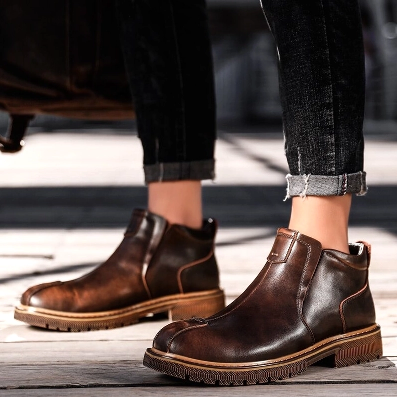 Mann trägt braune Gothic Chelsea Stiefel mit hochgekrempelten dunklen Jeans auf Holzflur, frontal stehende Casual Alternative Mode Pose