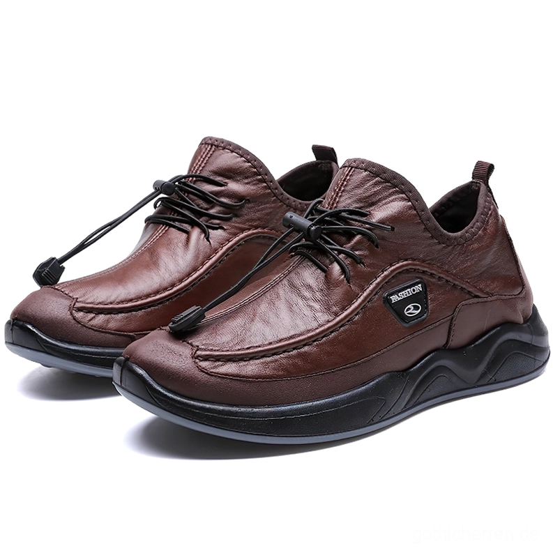 Braune Gothic-Kunstleder-Sneaker mit strukturierter Silhouette und welligem Schuhprofil, drei-Viertel-Vorderansicht mit minimalistischem Studiosetting