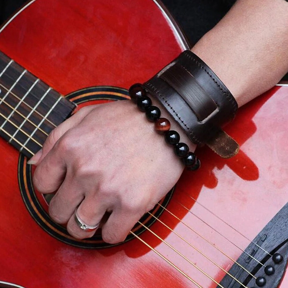 Männliche Hand trägt dunkles braunes Leder Gothic Armband am Handgelenk, neben roter akustischer Gitarre im Seitenprofil, getragen mit Perlenarmband und Silberring