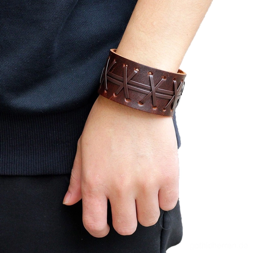Breites Leder-Gothic-Armband in Braun mit Kreuzstichmuster am Handgelenk getragen, zeigt natürliche Trageoptik und Druckknopfverschluss in alltäglichem Casual-Outfit-Setting