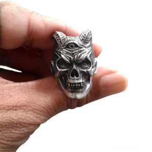 Dreiblickiger Dämonenschädel Ring mit gehörntem Design in antiker Silberfinish wird in Hand getragen - gotischer Edelstahl Bikerring mit scharfen Fangzähnen