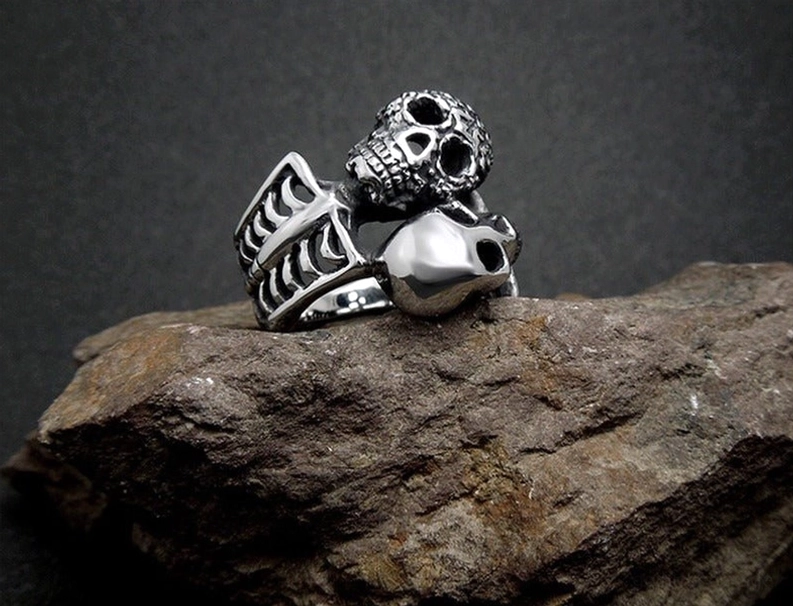 Vintage-inspirierter Doppelschädel Gothic Ring – Rückansicht auf dunklem Stein mit mattiertem gealterten Edelstahl-Finish, sichtbarer Skelett-Bandstruktur