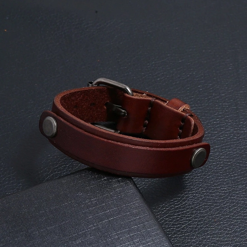 Dunkelbraunes echtes Leder Gothic Cuff Armband Wickeldesign mit Metallhardware auf strukturiertem Lederhintergrund