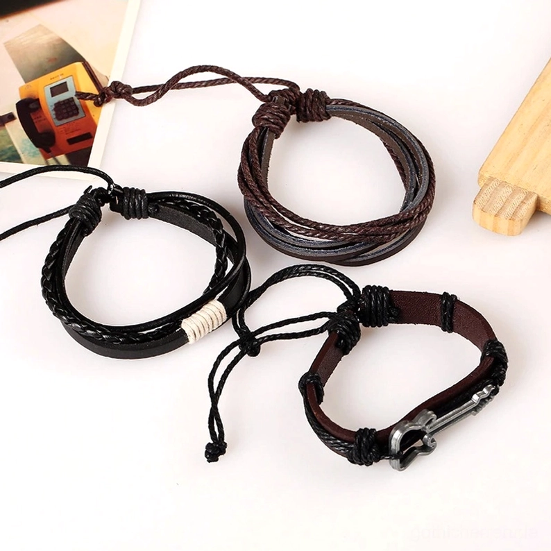 Vintage geflochtenes Kordel-Lederarmband mit Metallgitarren-Charm und verstellbarem Schnürenverschluss, Flachlage zeigt mehrlagige schwarze und braune Lederschichten mit Charm-Anhänger