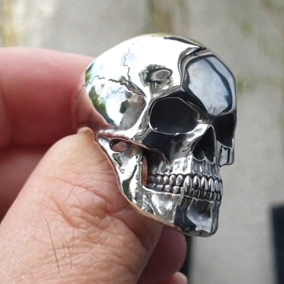 Silberner Totenkopf-Ring Dreiviertelperspektive am Finger getragen zeigt gerissene Schädeloberflächendesign polierte Oberflächenfinish und konvexe Konstruktion