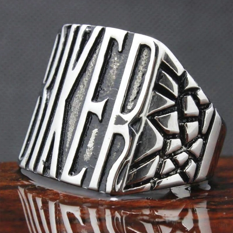 Gothic Biker Ring in schräger Winkelaufnahme mit geprägtem Text und strukturiertem Riss-Seitendesign, reflektierendem Holz-Hintergrund, detaillierte Ansicht