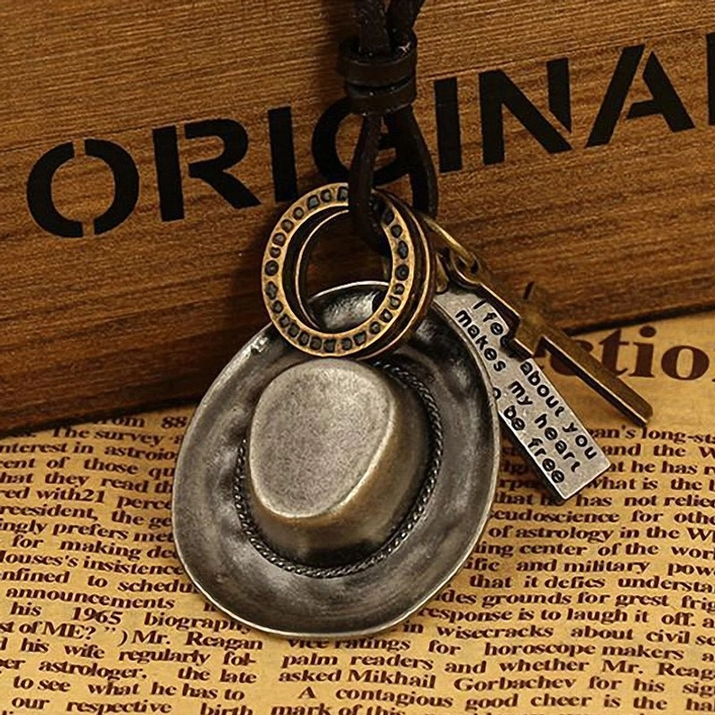 Antike silbergraue Cowboyhut-Anhänger auf dunklem Vintage-Hintergrund, gotische westliche Ästhetik Halskette mit vollständigen Charmdetails und Kettengestaltung