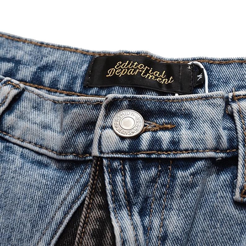Nahaufnahme der Taillenbund-Details an Gothic-Denim-Shorts mit Knopfleisten-Verschluss, gewebtem Brand-Label und goldfarbenen Kontrastnähten, Makro-Aufnahme