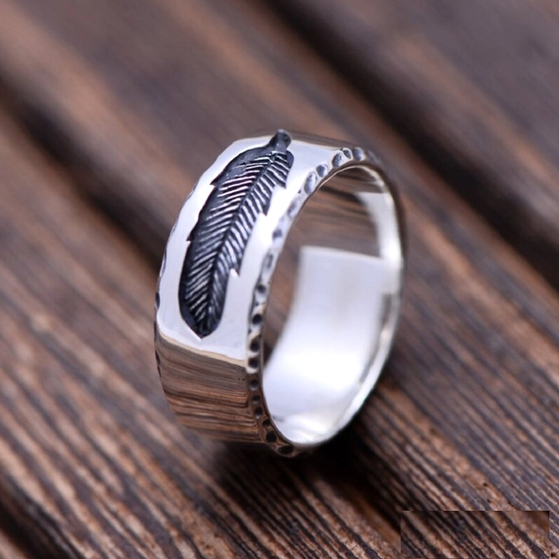 Linke 3/4 Perspektive des Vintage Gothic Federfeder Rings – schwarze gravierte Feder mit Punktrand auf poliertem Sterlingsilber auf Holzoberfläche