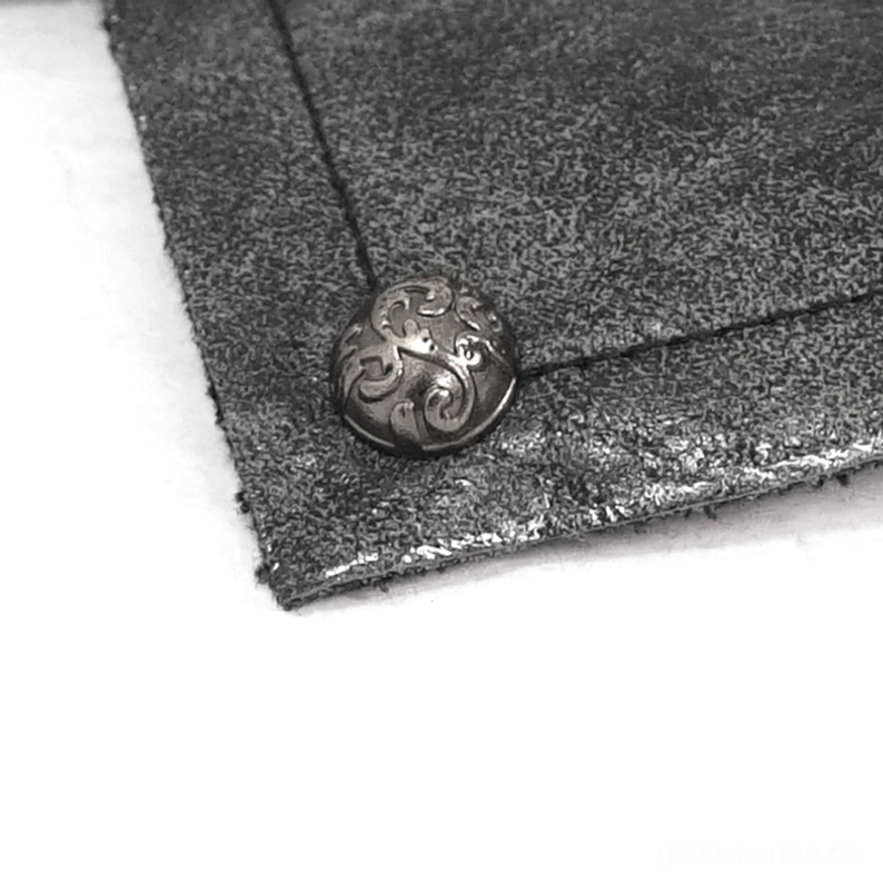 Makro-Texturaufnahme des Gothic-Handschuh-Materials mit eingeprägtem rundem Metallniete und matter distressierter schwarzer Lederoberfläche