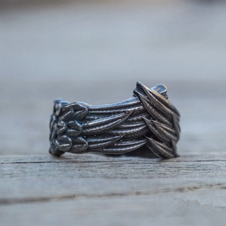 Dunkler Gothic Flügel Ring Frontalansicht auf Holzmaserung Hintergrund, symmetrische Federtextur und matte Edelstahl Material deutlich präsentiert
