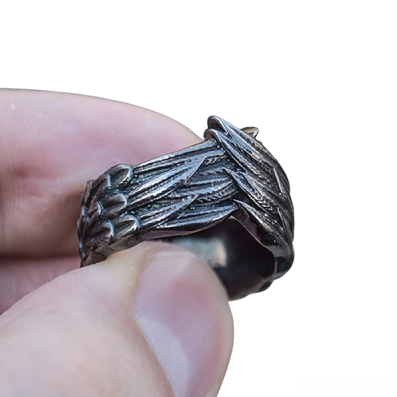 Nahaufnahme seitliche Detailansicht des dunklen Edelstahl Flügel Rings in Hand, geprägte Feder Aderntextur und gotische Ästhetik deutlich erkennbar