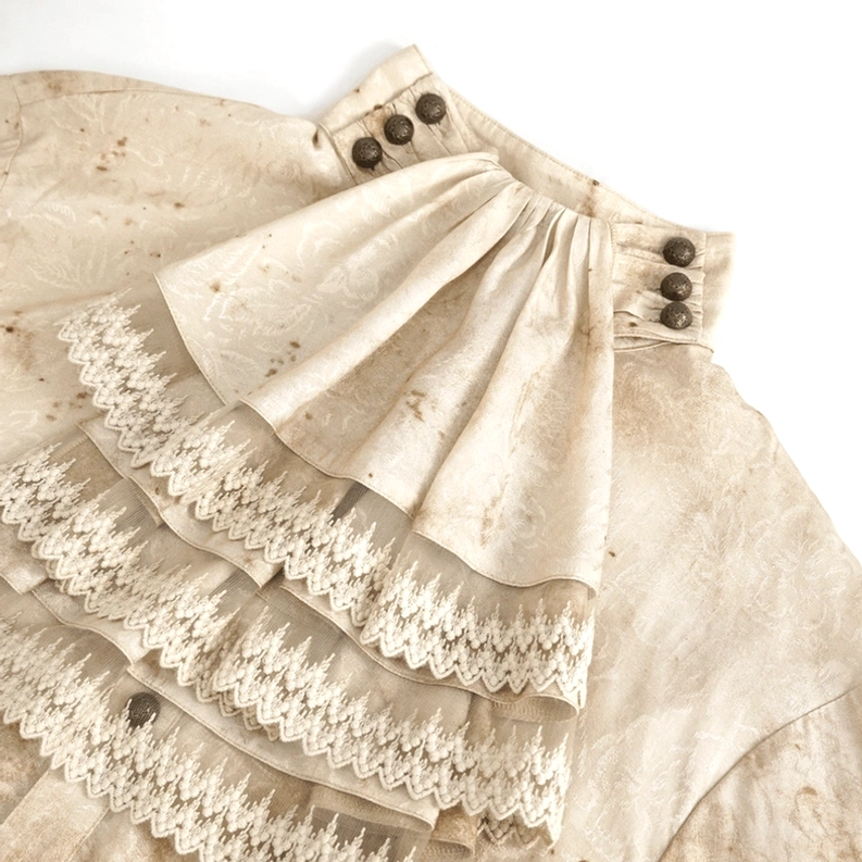 Nahaufnahme der mehrschichtig gerüsselten Spitzenkrawatte mit Metallkragenknöpfen, zeigt Gothic-Ästhetik und distressed beige gefleckte Stoff-Verwitterung