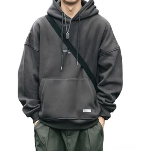 Oversized dunkelgrauer Gothic Letter Kapuzenpullover mit Drawstring-Kapuze, Drop-Shoulder-Design, Kangaroo-Pocket und großformatigem Brustgraphic auf männlichem Model in Vorderansicht – Premium Fleece Herren-Hoodie im Alternative Style