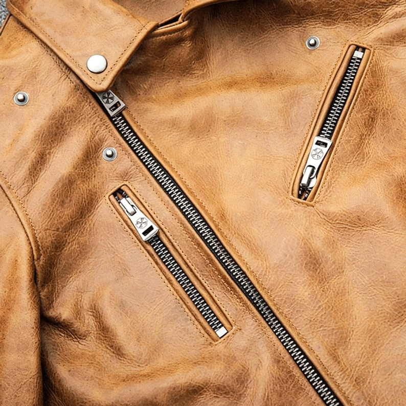 Detailansicht mehrfacher Reißverschluss-Taschen und silberner Akzente auf der distressed Camel Leder Motorradjacke mit industrieller Ästhetik