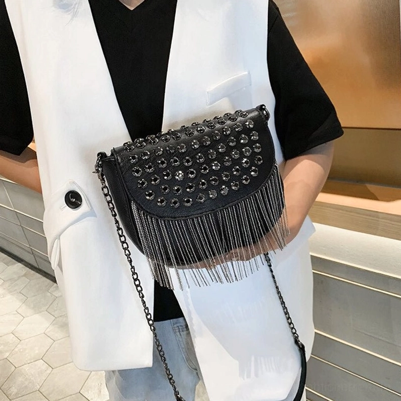 Frau stylt schwarze gotische Nieten-Schultertasche mit Kettenriemen, Vorderansicht-Dreiviertelseitenansicht im modernen Einzelhandelsraum mit Gothic-Umhängetasche