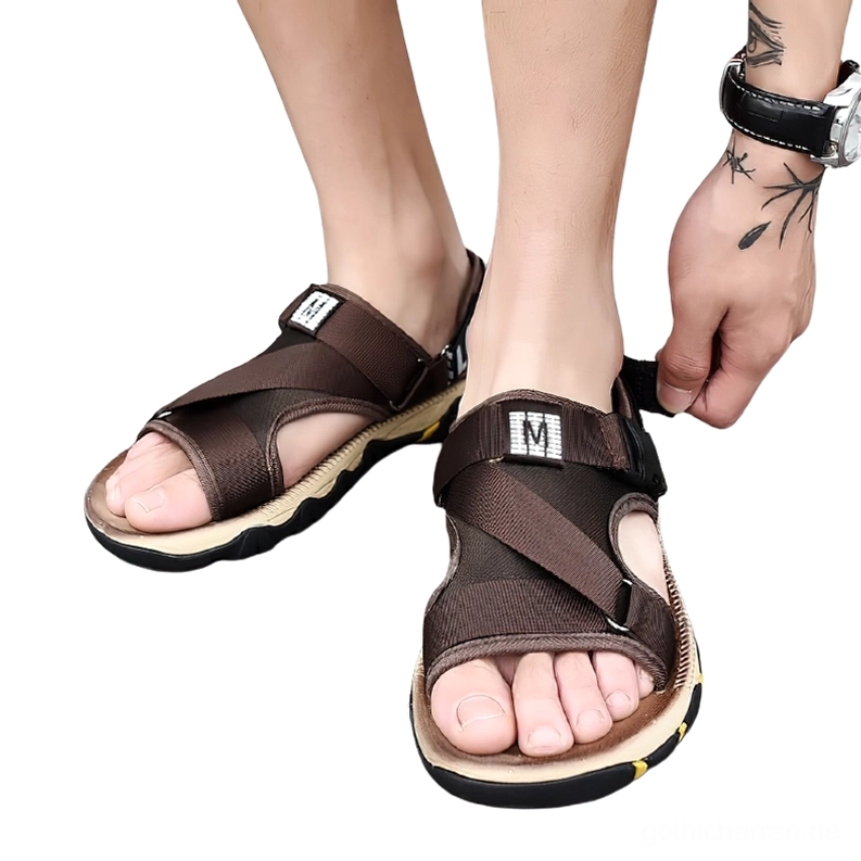 Männermodell trägt dunkelbraune Gothic Buckle Sandalen mit tätowierten Unterarmen, studiofotoaufnahme aus niedriger Perspektive zeigt schnallendetail beim anziehen