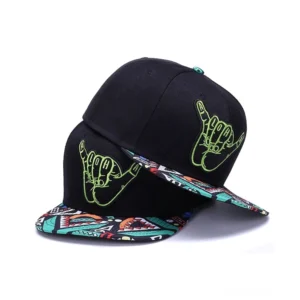 Gothic schwarze Snapback Cap mit neongrüner hand-bestickter Shaka-Hand-Logo und geometrisch gemustertem Schirm, schrägansicht von zwei übereinander gestapelten Kappen im Studio-Hintergrund