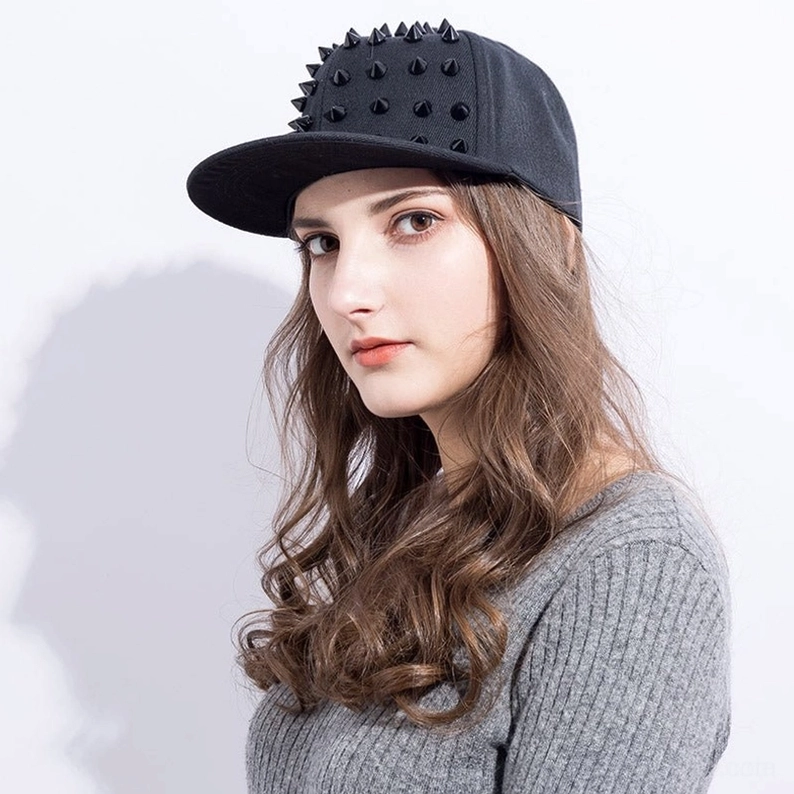 Modell trägt schwarze Spike Gothic Snapback Kappe mit silbernen Kegel-Nieten, kombiniert mit grauem Strickpullover für Goth-Styling