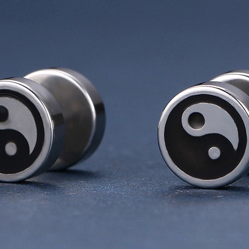 Paar Tai Chi Stecker-Ohrringe auf dunkeltürkisem Hintergrund, zeigt beide Ohrringe mit hochpoliertem Edelstahl-Yin-Yang-Muster und sicherer Druckfassung, Gothic minimalistischer Stil