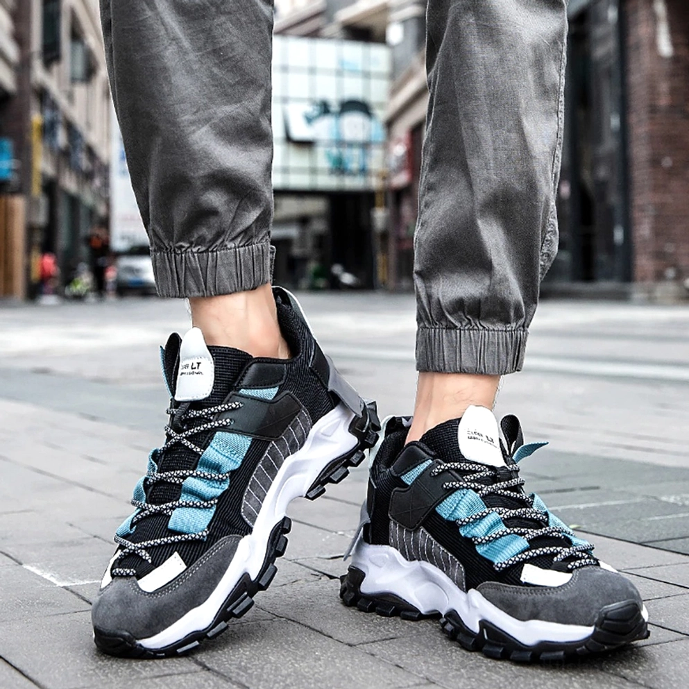 Männliches Modell trägt dunkle Gothic Lace-Up Turnschuhe mit grauen Casual-Hosen Augenhöhe-Straßenansicht urbaner Downtown-Stil