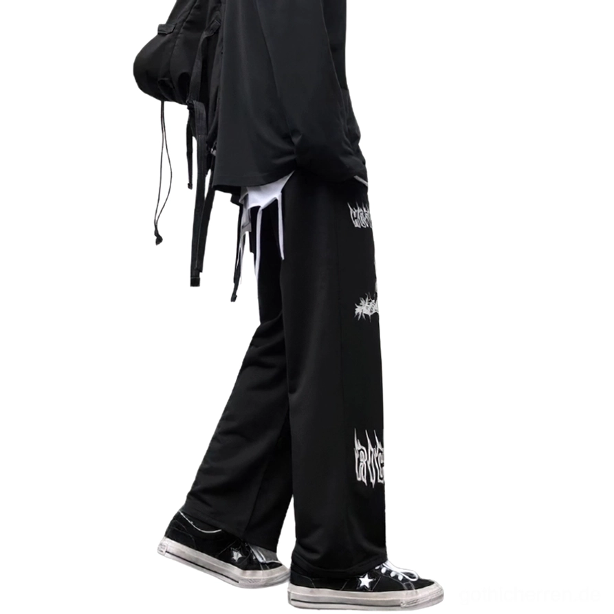 Männliches Model von hinten in schwarzer Gothic weiter Hose mit weißem Kreuz-Print, getragen mit schwarzem Rucksack und Layering, zeigt die vollständige Rückansicht und Drapierung