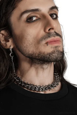 Gothic Vertebrae Choker in Seitenprofilansicht, getragen von langhaarigem männlichen Modell mit Federohrringen, studiohintergrund zeigt die Seitenkrümmung und Wirbelketten-Details