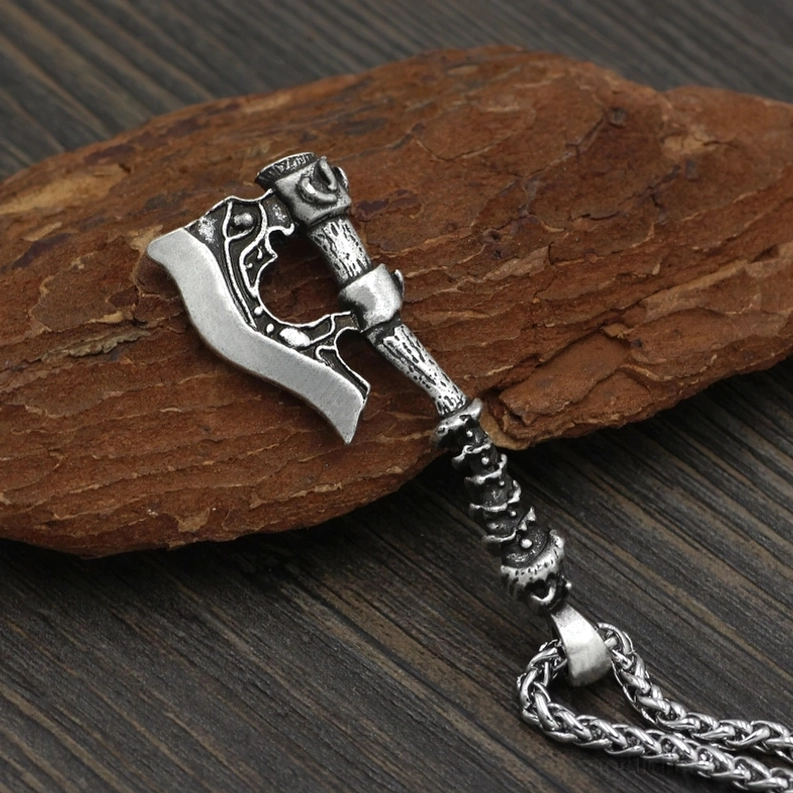 Silberner gotischer Viking-Axt-Anhänger-Halskette mit geschnitzten Details und Schiebeperlenelement auf Kette, schräge Seitenansicht auf Holz-Rinde-Hintergrund