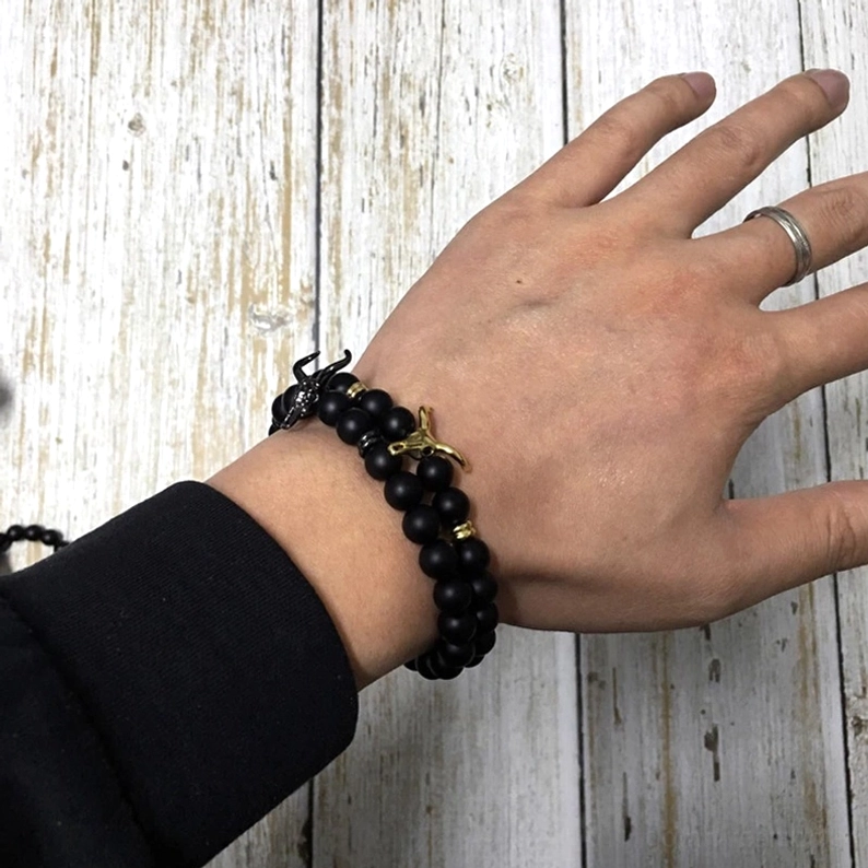 Mann trägt Gothic schwarzes Stein-Stier-Amulett Perlenarmband mit goldenem Akzent am Handgelenk, Styling-Anleitung für alternative Herren-Schmuck