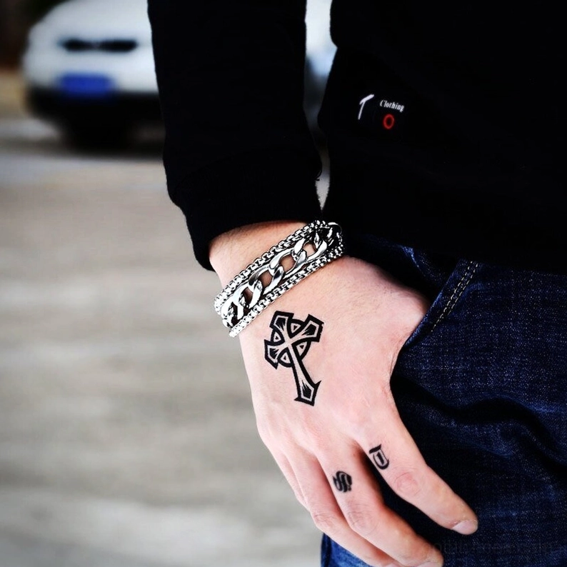 Doppelschicht-Edelstahl-Armband am tätowierten männlichen Handgelenk getragen im Freien, Seitennahaufnahme mit Straßenhintergrund, silberpolierte Punk-Ästhetik des Gotik-Schmucks