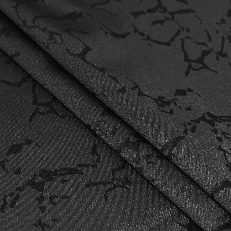 Nahaufnahme Detail schwarze Jacquard Gewebetextur mit gothischem Floralmuster, Prägemuster auf feinem Satinstoff, Lichbrechung zeigt dreidimensionale Strukturtiefe