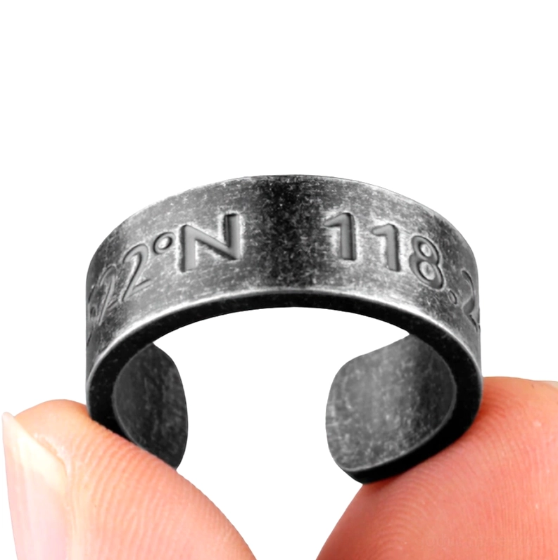 Offener Gothic Koordinaten-Manschetten-Ring an Finger getragen, Nahaufnahme zeigt Koordinaten-Gravur, dunkles antikes Metallfinish und flexible Manschetten-Passform, Close-up der Ringoberfläche mit präzisions-eingravierter Koordinaten-Inschrift