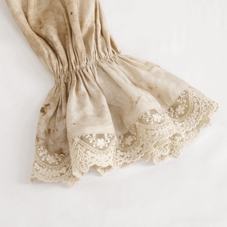 Nahaufnahme der Laternenmännchen-Manschette mit elastisch geraffter Spitzensaum und besticktem Spitzendetail auf distressed beigem Jacquard-Stoff, handgefertigte Spitzenarbeit