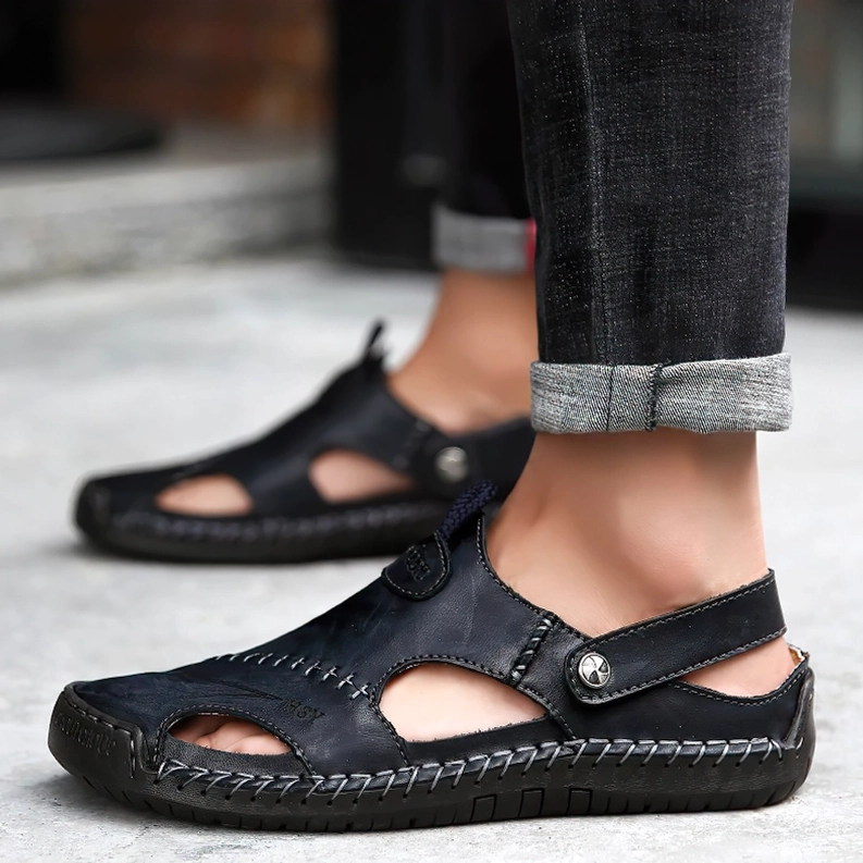 Männliches Modell trägt schwarze Leder-Gothic-Buckle-Sandalen mit beiden Füßen sichtbar auf Pflastersteinen, Outdoor-Lifestyle-Aufnahme – Dark Fashion Herren-Schuhwerk