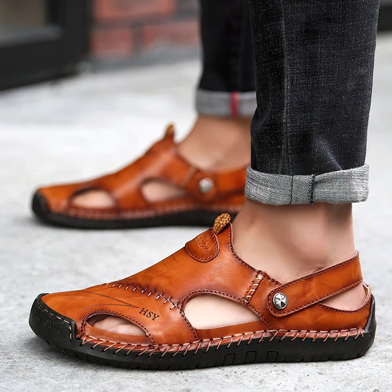 Mann in hochgerollter Jeans trägt hellbraun-Tan farbene Leder-Gothic-Sandalen mit geschlossener Zehenkappe auf Outdoor-Straße – Alternative Herren-Footwear