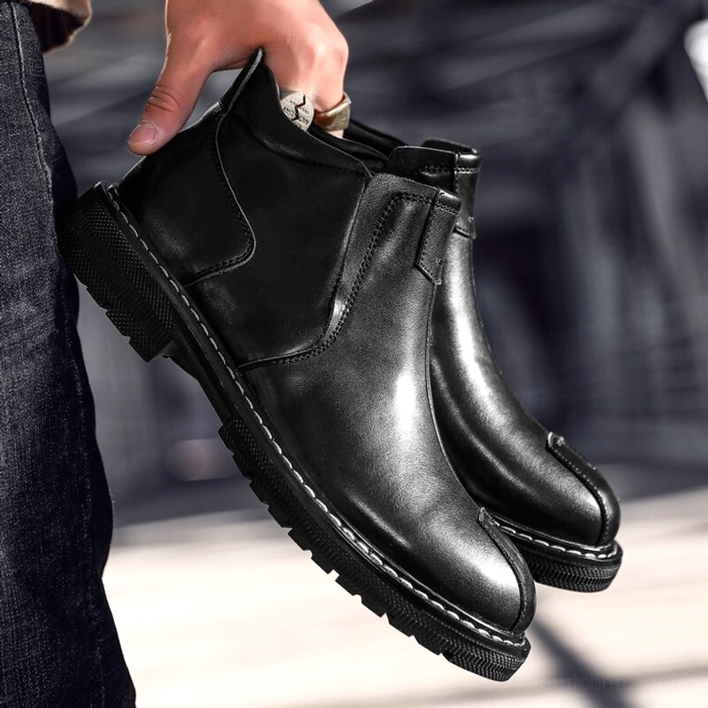 Mann trägt schwarze Gothic Chelsea Leder-Stiefel mit hochgekrempelten dunklen Jeans, urbane städtische Außenszenerie, tiefe Frontansicht, alternative Mode Styling