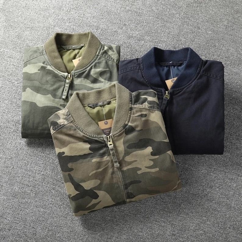 Mehrere Farb-Varianten Military Camo Denim Bomberjacken zusammengefaltet, Vogelperspektive zeigt Dschungel-Grün, helles Tarn und Navy Optionen