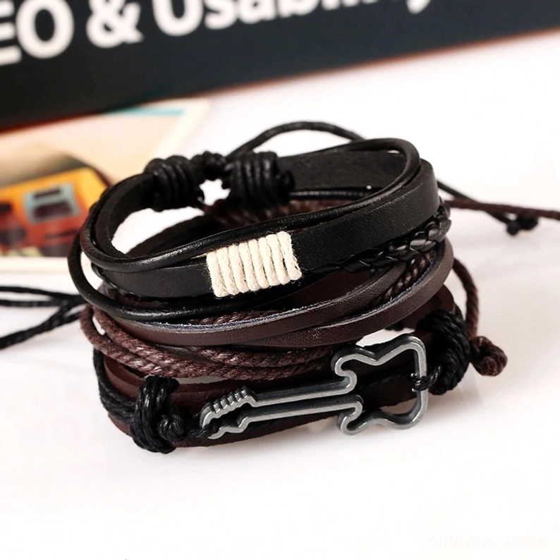 Mehrlagiges Vintage Gothic Lederarmband mit gewebtem Stoffdetail, Metallgitarren-Charm-Anhänger, mehrschichtige braune und schwarze Ledertöne in Flachlage auf dekorativem Untergrund
