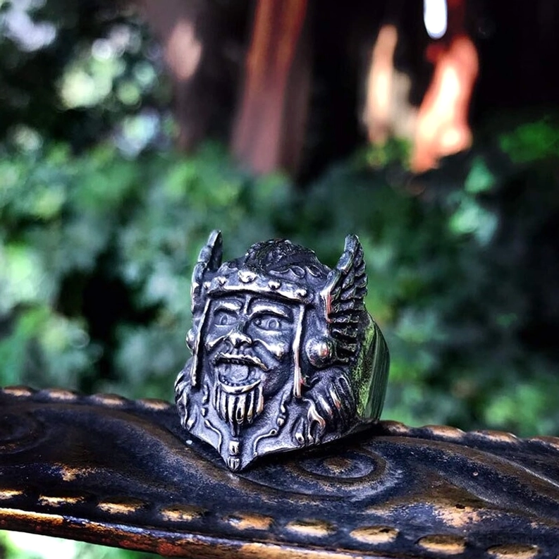 Odin Gothic Ring Nahaufnahme Vorderansicht mit dunkel vintage-silbernem Edelstahl, Außensetting mit grünem Laub und Naturhintergrund, geflügelter Helm Krieger-Schnitzwerk, authentische Outdoor-Darstellung