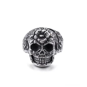 Ornater Totenkopf-Ring mit Blüten-Motiven aus Silber-Edelstahl, vordere Ansicht, geprägte Blumenmuster um die Schädelform, gotisches Memento-Mori-Schmuckstück, detaillierte Blüten- und Knochenlinien, Statement-Ring für Alternative-Fashion