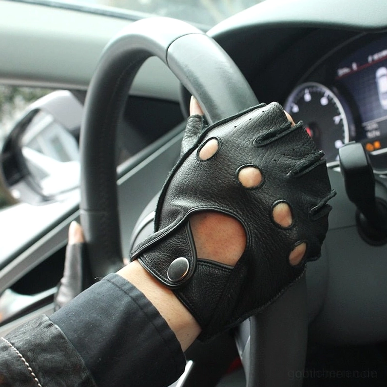 Schwarze fingerlose Lederhandschuhe mit Druckknopf-Verschluss, an männlicher Hand in Auto-Innenraum, Gothic half-finger Handschuhe in Fahrerposition