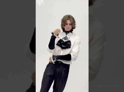 Männliches Goth-Model, das schwarze Samtarmschuhe als Teil eines vollständigen formalen Goth-Outfits trägt, mit hochsitzenden Hosen und passenden Accessoires, dreiviertelseitige Studio-Aufnahme mit grauem Hintergrund