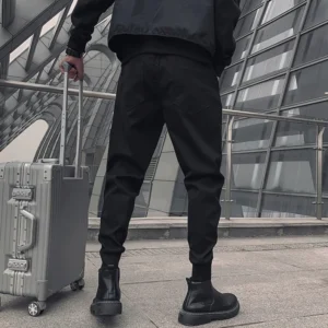 Schwarze Cargo-Hose Rückansicht im modernen Außenbereich mit Rollkoffer im Urban-Reise-Stil