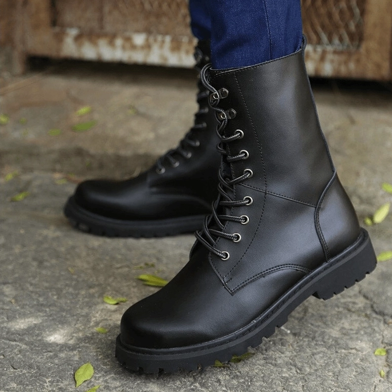 Schwarze Gothic Combat Boots am Modell getragen, Outdoor Street-Wear Ansicht mit blauen Jeans, niedrige Seitenansicht der dicken Gummisohle