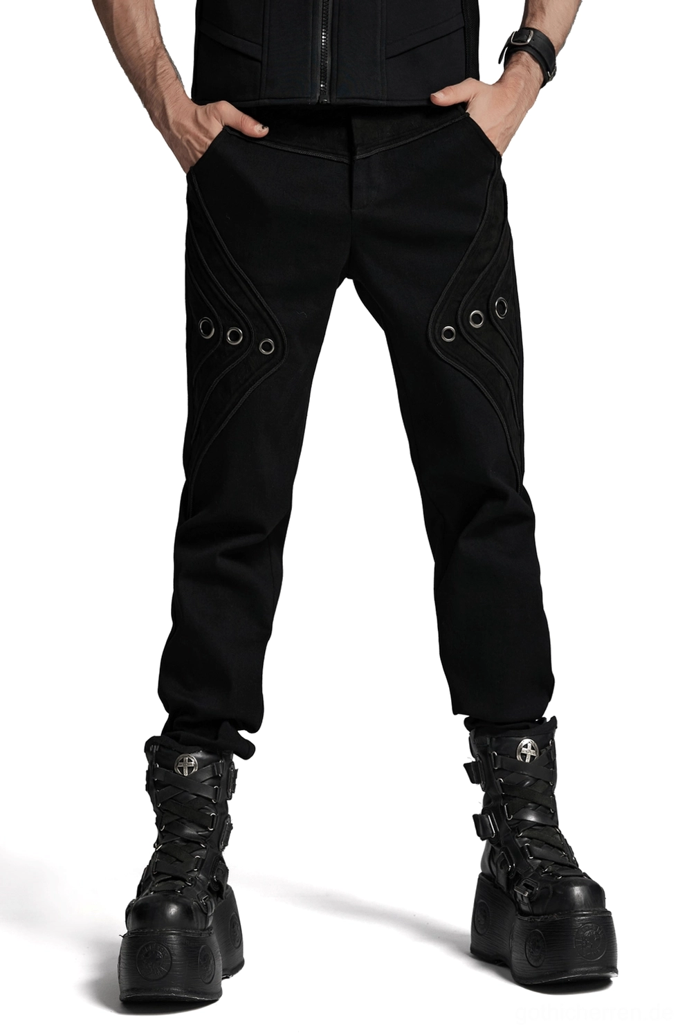 Schwarze Gothic-Denim-Hose mit Metall-Ösen an beiden Oberschenkeln, getragen von männlichem Model in Frontansicht mit schwarzer Weste und Platform-Skull-Boots im Studio