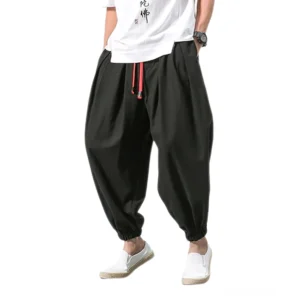 Schwarze Gothic Haremshose für Herren mit rotem Kordelzug und elastischen Knöchelbündchen, Vorderansicht auf männlichem Model, lockerer Schnitt Pluderhose Darkwear