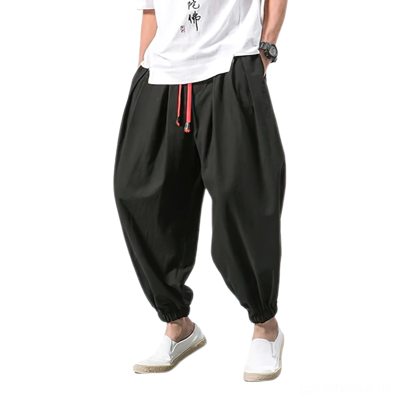 Schwarze Gothic Haremshose für Herren mit rotem Kordelzug und elastischen Knöchelbündchen, Vorderansicht auf männlichem Model, lockerer Schnitt Pluderhose Darkwear